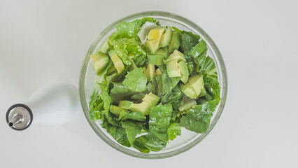 Romaine lettuce, celery, and avocado salad in a glass bowl on white kitchen table, view from above