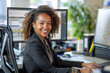 © Kowit - a businesswoman at her desk, framed by monitors, exuding confidence and warmth in a bright office setting.