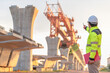 © reewungjunerr - An Asian male engineer works at a motorway bridge construction site,Civil worker inspecting work on crossing construction,Supervisor working at high-speed railway construction site
