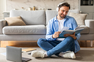 Poster - A man is seated on the floor, engrossed in reading a book while simultaneously listening to music through headphones. He appears focused and relaxed in his dual activities.