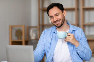 Aufkleber - A man is seated at a desk, using a laptop while sipping on a cup of coffee. He appears focused on his work, surrounded by a simple office setting.