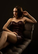 © Dimid - A beautiful sexy girl in a leather dress sits on a sofa on a black background.