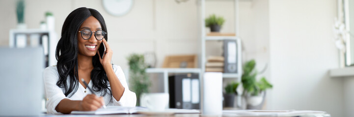 Aufkleber - Happy young black woman in formal wear talking on smartphone at workplace, copy space. Beautiful African American business lady having phone conversation with partner or colleague, copy space