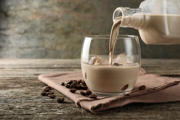 Wall Mural - Pouring coffee cream liqueur into glass at wooden table, closeup