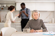 © JackF - Competitive middle-aged man and woman conflicting and old woman writing testament sitting at kitchen table