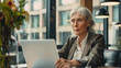 © kanesuan - Mature woman using a non-Apple laptop in a well-lit, modern office