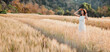 © Satori Studio - A woman is standing in a field of tall golden wheat. She is wearing a white dress and a straw hat
