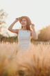 © Satori Studio - A woman wearing a straw hat stands in a field of tall grass. She is smiling and she is enjoying the moment