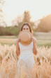 © Satori Studio - A woman is standing in a field of tall grass, holding a straw hat over her face. The scene is serene and peaceful, with the sun shining down on the woman and the grass
