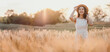 © Satori Studio - A woman is standing in a field of tall golden grass, wearing a straw hat and smiling. Concept of peace and tranquility, as the woman is enjoying the simple beauty of nature