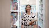 Fototapeta  - A girl is smiling and holding a stack of books in a library