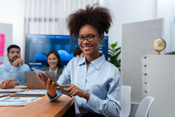 Wall Mural - Happy young african businesswoman wearing glasses portrait with group of office worker on meeting with screen display business dashboard in background. Confident office lady at team meeting. Concord