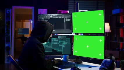 Wall Mural - Hacker developing spyware software on green screen computer to steal important data to be sold on black market. Hooded scammer writing malicious code on chroma key PC, camera B