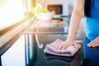 © sorapop - Young housewife smiles while disinfecting her kitchen table with a rag and detergent. Emphasizing routine cleaning and care for a sanitized living space. Wiping cloth kitchen