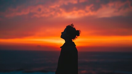 Canvas Print - Young woman standing alone on a beach watching a beautiful sunset. She is lost in thought, contemplating her life and her future.