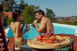 Fototapeta  - Couple enjoying their fruit cocktails by a swimming pool