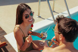 Fototapeta  - Couple sitting by the pool, having drinks and eating fruit