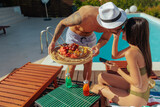Fototapeta  - A man leaning in for kiss while serving food to woman by a poolside