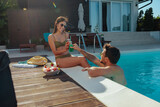 Fototapeta  - Wide shot of a two people having drinks by a swimming pool