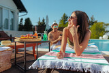 Fototapeta  - A woman in sunglasses laughing on a sun lounger by a pool