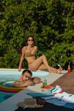 Fototapeta  - Woman sitting by a pool posing and man relaxing on a float.