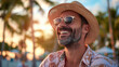 © boxstock production - Cheerful man wearing straw hat and sunglasses smiling with sea breeze on sandy beach at early sunrise