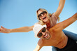 © peopleimages.com - Couple, sunglasses and piggyback on vacation, holiday and peace or flying game by blue sky. People, below and mockup space for bonding on weekend, outdoor nature and love for marriage or romance