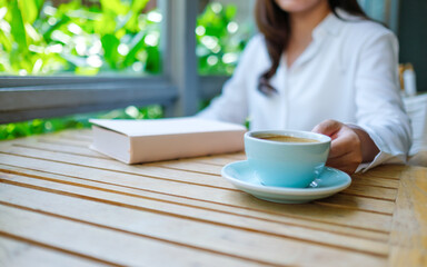 Wall Mural - Closeup image of a woman drinking coffee with a book on table