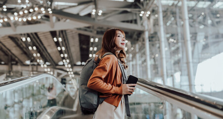 Wall Mural - Young asian woman in international airport terminal or modern train station. Backpacker passenger female commuter walking on escalator