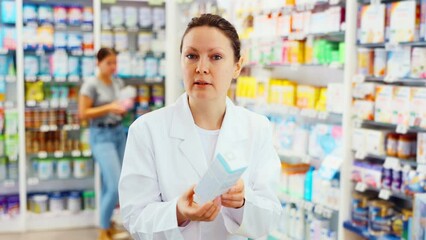 Wall Mural - Young female pharmacist posing with remedy in pharmacy. High quality 4k footage