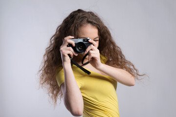 Wall Mural - Portrait of a gorgeous teenage girl with curly hair holding camera. Studio shot, white background with copy space