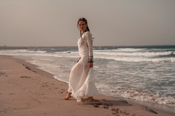 Wall Mural - Model in boho style in a white long dress and silver jewelry on the beach. Her hair is braided, and there are many bracelets on her arms.