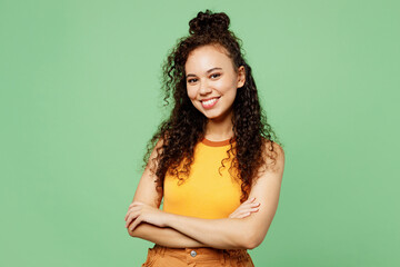 Wall Mural - Young smiling cheerful woman of African American ethnicity wear yellow tank shirt top hold hands crossed folded look camera isolated on plain pastel light green background studio. Lifestyle concept.