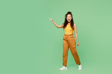 Wall Mural - Full body young woman of African American ethnicity wears yellow tank shirt top walk go point index finger aside on area isolated on plain pastel green background studio portrait. Lifestyle concept.