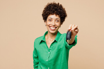 Poster - Young smiling fun woman of African American ethnicity wear green shirt casual clothes hold in hand car key fob keyless system isolated on plain pastel light beige background studio. Lifestyle concept.