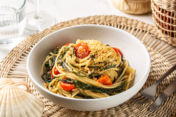 Wall Mural - Spaghetti with agretti, or salsola soda, tomatoes, bread crumbs, pinoli pine nuts and anchovy in a white plate. Italian pasta, white dinner table.