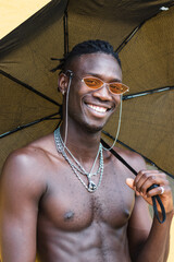 Portrait handsome African American man shirtless holding an umbrella. Black man with stylish sunglasses smiling at camera