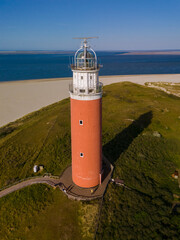 Poster - An aerial perspective capturing a lone lighthouse standing tall on the sandy shore of Texel, Netherlands, guiding ships safely through the night.