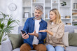 © Liubomir - Mature couple having a serious discussion about smartphone issues while sitting on a comfortable sofa in their modern living room.