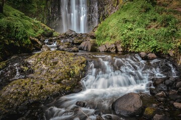 Natural, scenic landscape of a waterfall flowing out of rocky terrain in a wooded area