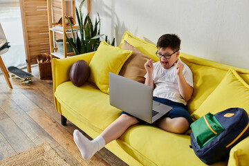 Wall Mural - A adorable boy with Down syndrome sitting on a yellow couch, using a laptop.