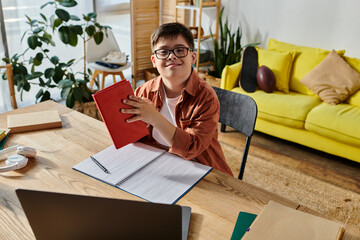 Wall Mural - A boy with Down syndrome seated at a desk, focused on his notebook and laptop.