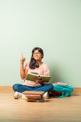 Indian asian school girl in casual wear reading book while sitting on floor