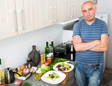 Fototapeta Koty - Positive guy stands proudly in kitchen hands clasped