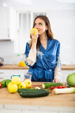 Fototapeta Koty - Satisfied woman in dressing gown eating apples in kitchen during breakfast