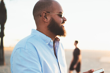 Fototapete - Bearded man sending text message via mobile telephone chatting online while enjoying summer evening, hipster guy satisfied with 4G connection in roaming share photos from vacation in social networks