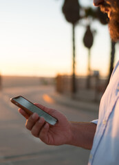 Fototapete - Cropped image of bearded male holding mobile phone reading news information from browsed web page standing on street,hipster guy viewing photos in social networks blogging online via smartphone