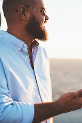 Fototapete - Happy young male in sunglasses holding smartphone in hands using good internet connection during leisure outdoors, smiling hipster guy looking away waiting for income message on cellular application
