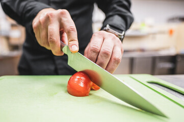 Wall Mural - A person slices a tomato on a green cutting board using a kitchen knife.