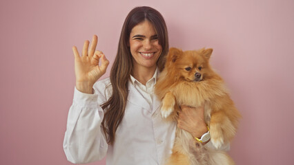 Sticker - Smiling woman holding pomeranian dog against pink background showing okay sign with hand